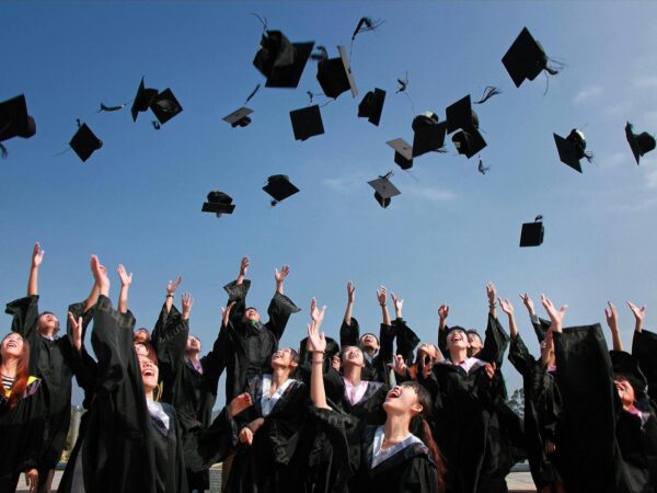 newly graduated people wearing black academy gowns throwing hats up in the air