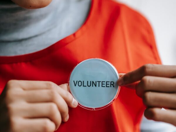 smiling ethnic woman showing volunteer sign on red apron