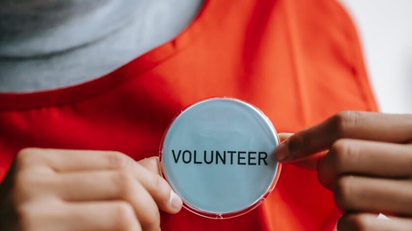 smiling ethnic woman showing volunteer sign on red apron