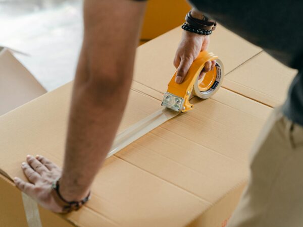crop faceless man packing box with scotch tape