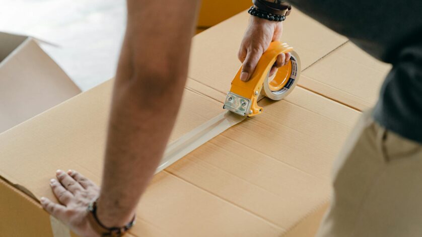 crop faceless man packing box with scotch tape