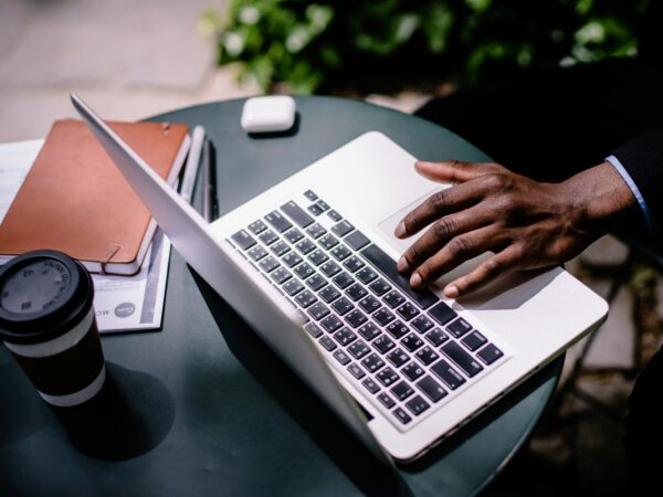 crop unrecognizable black businessman typing on laptop in street cafe