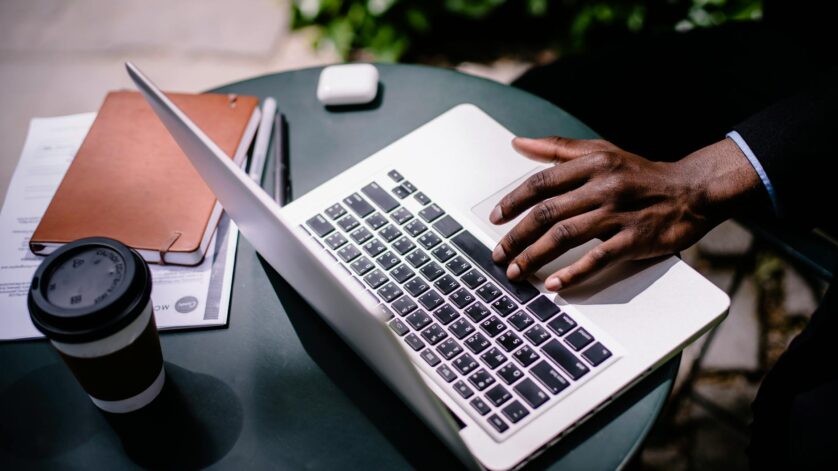crop unrecognizable black businessman typing on laptop in street cafe