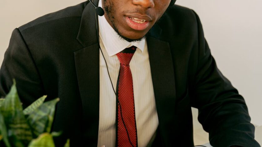 man in black suit writing on a notebook while seriously looking at the camera
