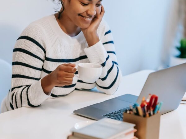 smiling young ethnic woman working distantly on laptop and talking on smartphone