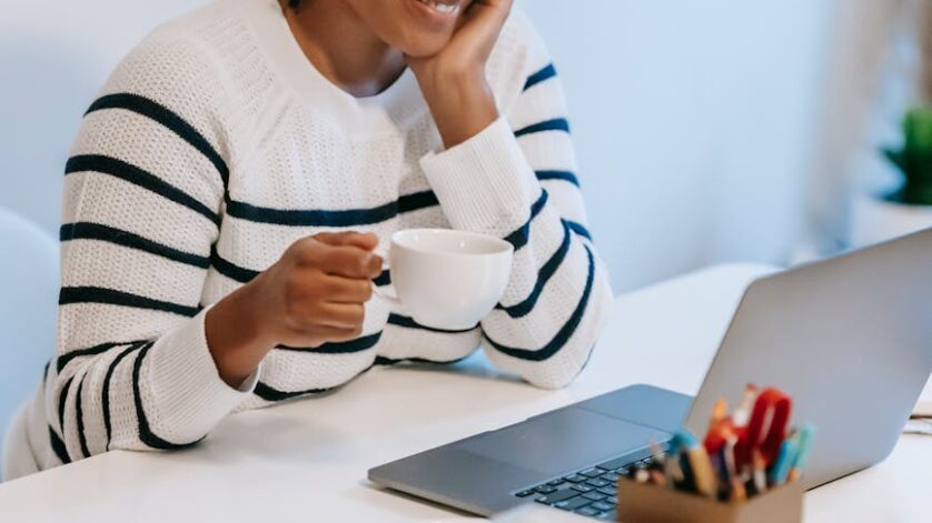 smiling young ethnic woman working distantly on laptop and talking on smartphone
