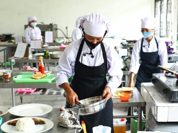 a person in white chef hat and black apron holding stainless steel bowl