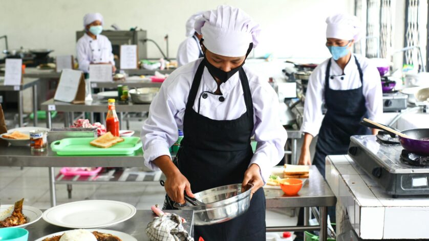 a person in white chef hat and black apron holding stainless steel bowl