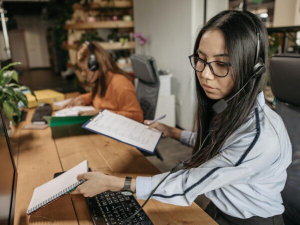 woman wearing headset holding notebook and a clipboard