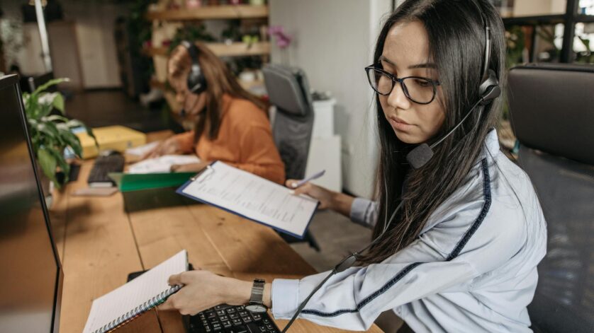 woman wearing headset holding notebook and a clipboard